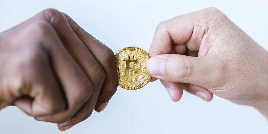 close up view of two people's hands holding a gold bitcoin together